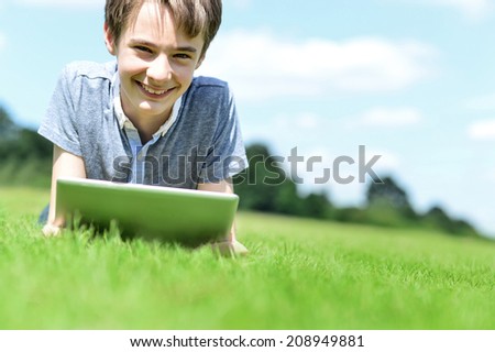 Smiling boy lying on grass and using his tablet pc