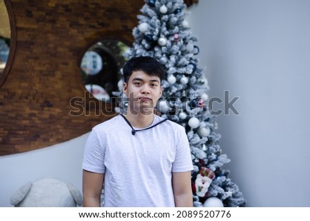 young asian man with white t-shirt stand in front of white christmas tree as background