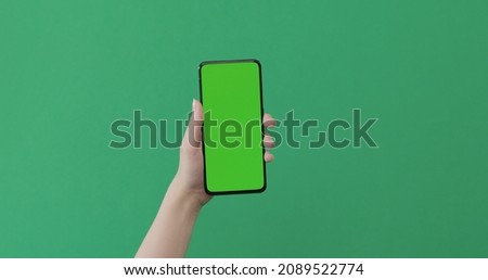 Young female hand hold smartphone with green screen on green background