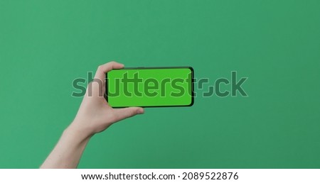Young man hand hold smartphone with green screen on green background