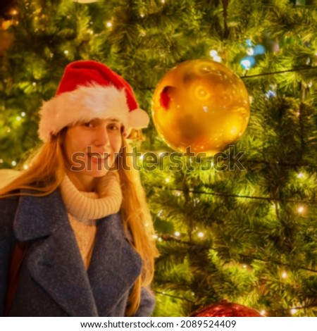 Blurred image of a girl in a Santa hat near a Christmas tree with large balls. Defocused picture. Blur focus