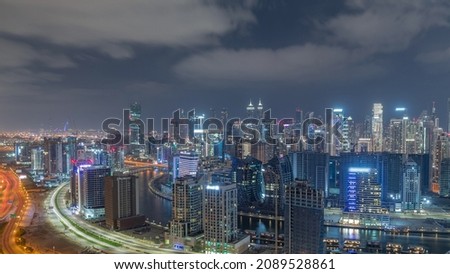 Skyline with modern architecture of Dubai business bay illuminated towers during all night panoramic timelapse with lights turning off. Aerial view with canal and construction site