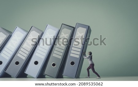 Many ring binders with tax documents and bills falling over a scared businesswoman Royalty-Free Stock Photo #2089535062