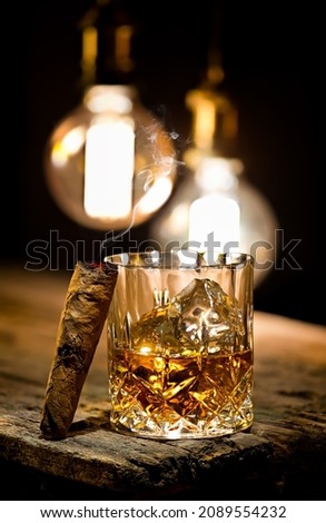 Cigar and glass with whiskey with ice cubes