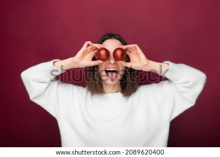 Isolated young girl shows her tongue and holding 2 Christmas balls near her eyes