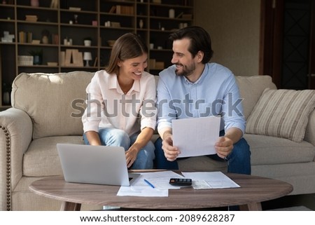 Happy couple of tenants, homeowners doing domestic paperwork, reading paper documents, using laptop computer, calculating expenses, paying bills, insurance, mortgage fees on internet with online app Royalty-Free Stock Photo #2089628287
