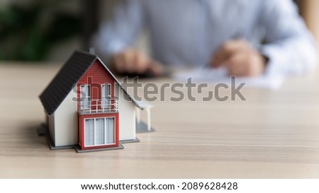 On blurred background, client sits at table signing rental agreement or purchasing contract, close up to cottage house layout. New built house offer, affordable dwelling, real-estate agency ad concept
