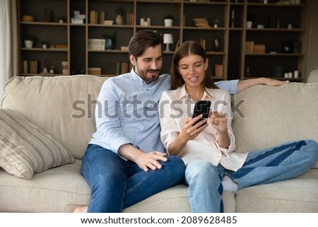 Happy millennial couple using online shopping app, internet service, making video phone call, sharing cellphone, watching media content together, talking, resting on sofa with digital device at home Royalty-Free Stock Photo #2089628485