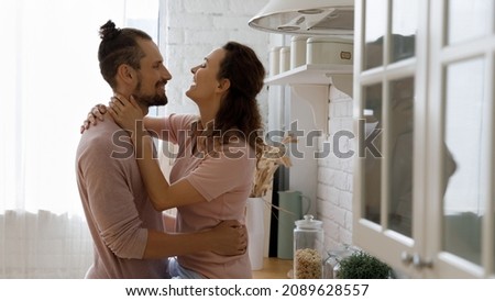 Happy millennial married couple in love hugging in kitchen, enjoying romantic leisure time together at home. Dating girl and guy hugging, kissing, talking, laughing in domestic interior. Banner