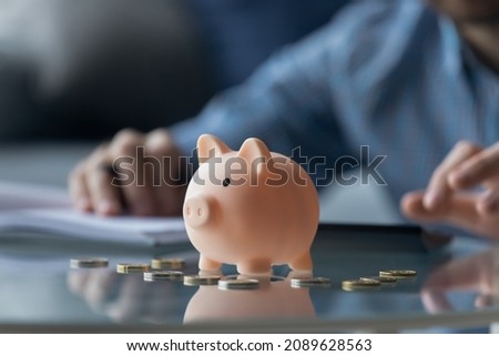Pink piggy bank euro coins on table, close up view, man on background calculates expenses, managing finances, household bills or taxes, save money for future, take care for tomorrow, frugality concept Royalty-Free Stock Photo #2089628563