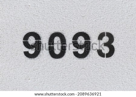 Black Number 9093 on the white wall. Spray paint. Number nine thousand ninety three.
