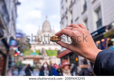 Hand holding a french macaroon cookie (Macaron) on the street of Paris near Sacre Coeur cathedral. Delicious, sweet meringue sandwich or confection.