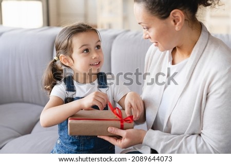 Caucasian young mother unwrapping opening unpacking birthday Christmas New Year Mother`s day present with her small daughter child girl. Family celebration holiday