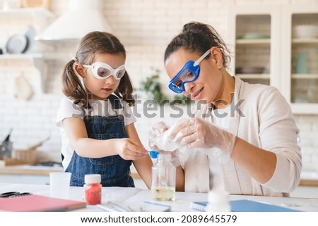 Scientific experiment at home. Laboratory tests for school homework. Parent mother with daughter kid making chemical test at home kitchen. Nanny babysitter teacher help in protective glasses Royalty-Free Stock Photo #2089645579