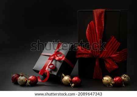 Composition of gifts of different shapes wrapped in black wrapping paper with a red ribbon and a bow on a black background. Side view. Copy space.