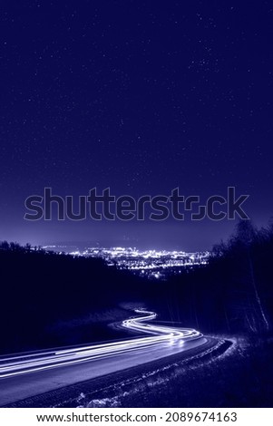 Starry sky above city lights and light trails. Night photography, toned in trendy Color Of The Year 2022 - Very Peri