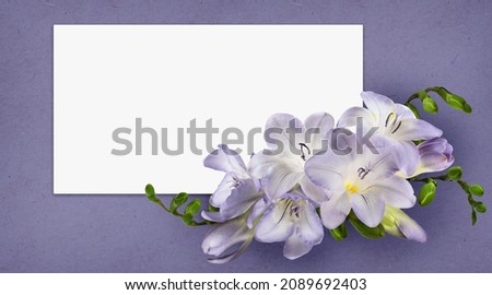 Purple freesia flowers in a floral arrangement with white card on textured paper background