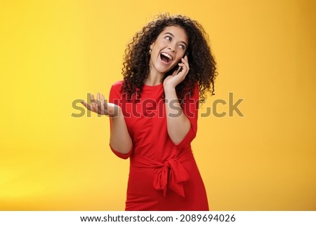 Talkative glamour silly girl with curly hair having fun feeling carefree and happy taling on mobile phone turning away as laughing joyfully gesturing with hand holding smartphone pressed to ear Royalty-Free Stock Photo #2089694026
