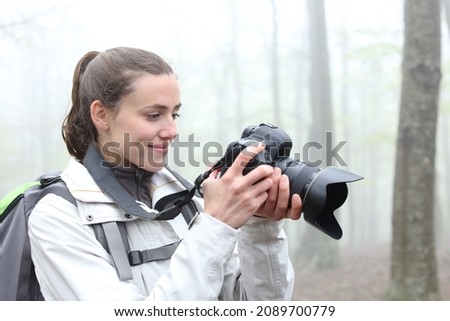 Hiker checking photos on dslr camera waking in a foggy forest