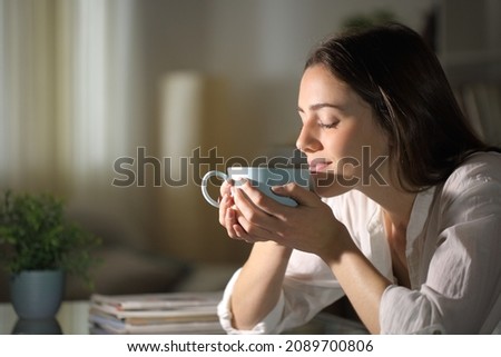 Relaxed woman smelling coffee in the morning sitting in the living room at home Royalty-Free Stock Photo #2089700806