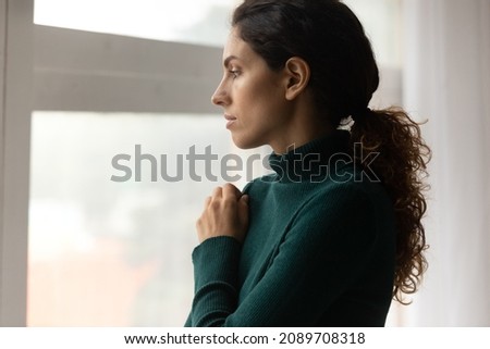 Sad millennial woman look in window distance thinking pondering of life problems. Unhappy young Hispanic female feel lonely depressed on lockdown or quarantine at home. Depression, anxiety concept.