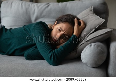 Upset millennial Latino woman lying on couch at home feel depressed with life problems troubles. Unhappy young Hispanic female rest on sofa distressed with abortion or miscarriage. Drama concept. Royalty-Free Stock Photo #2089708339