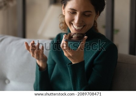 Close up of smiling young Latin woman use cellphone record audio message talk on loudspeaker online. Happy Hispanic female activate digital voice assistant on smartphone. Communication concept.