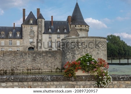 Looking across a moat at a old castle with beautiful brightly coloured flowers in the foreground