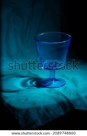 A glass blue vase stands on a table on a dark blue blurred background in the evening light.