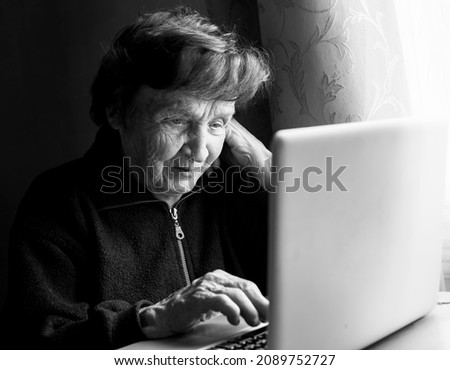 Old woman studying working on the computer in her home. Black and white photo.