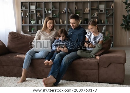 Addicted to modern technology happy bonding young couple parents and little cute children siblings using different gadgets, playing games, spending time online in social networks or shopping.