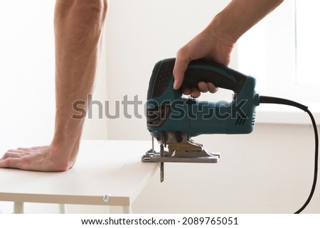 close up Carpenter is sawing a plywood sheet with jig saw machine. Side view. Royalty-Free Stock Photo #2089765051