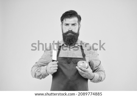 brutal cook cut tomato. man in apron with long beard. handsome confident guy cooking vegetable food. healthy eating and diet. hunting on vitamins. bearded chef wearing red apron
