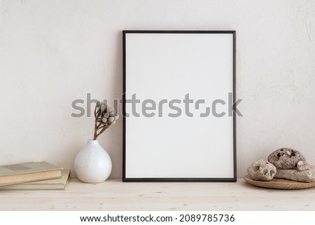 White desk with photo frame and  minimal round vase with a decorative twig and books against bright wall. 