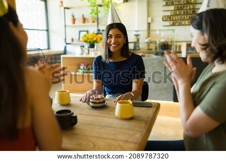 Celebrating together! Best friends clapping while singing happy birthday to a young woman at a restaurant 