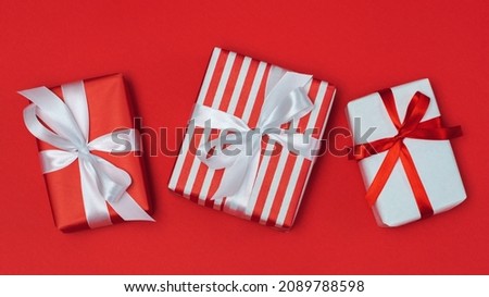 Above view composition of three present boxes decorated with wrapping paper and satin ribbons bows, isolated over red background.