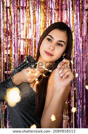 New Year party celebration. woman in glitter dress holding christmas lights, romantic look on purple and gold glitter background