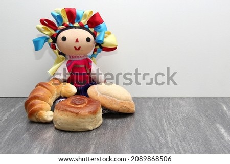Freshly baked Mexican sweet bread omo croissant, cuernito, eye of pancha, bisquet, biscuit and worm on a table next to a handmade Mexican doll combed with colored ribbons
