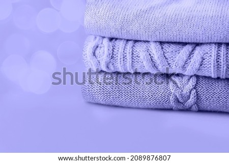 A stack of cozy winter autumn sweaters in lavender tones on a color close to lovender background. Knitted wool sweaters. Fashion style. Copy space. Color of the year very peri.
