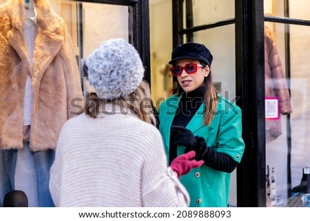 Young blonde girl shopping in the city and served by a shop assistant, looking at shop windows of clothing stores. Sunglasses and red gloves