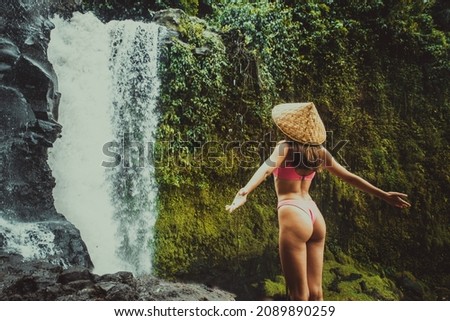 Beautiful young woman posing at the great Tegenungan waterfall in the deep rainforest of Bali island, Indonesia.