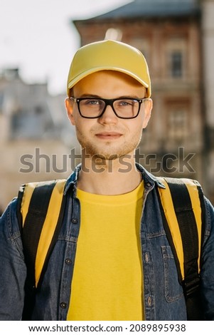Portrait of a young delivery man who is standing and smiling. He is wearing yellow clothing. Center of the old city. Vertical photo.
