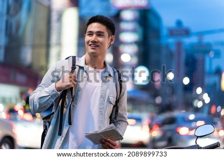 Asian attractive man backpacker walking around the city at night road. Young handsome guy tourist traveler travel alone on street use map to find destination, enjoy spend time on holiday vacation trip Royalty-Free Stock Photo #2089899733