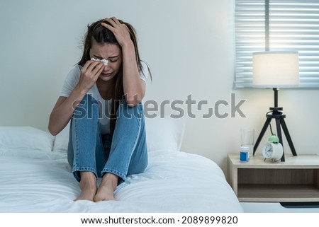 Asian beautiful depression girl crying in tears sit on bed in bedroom. Attractive unhappy young woman feeling sad lonely and upset with life problem and hold tissue on hands in dark night room at home Royalty-Free Stock Photo #2089899820