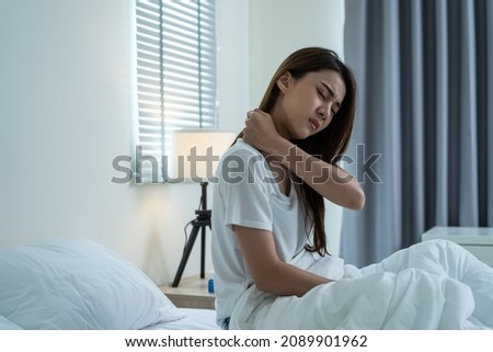 Asian beautiful sick girl in pajamas getting up from sleep in bedroom. Unhappy young woman feel bad and painful after wake up on bed, having backache then press hands to massage lower back at night. Royalty-Free Stock Photo #2089901962