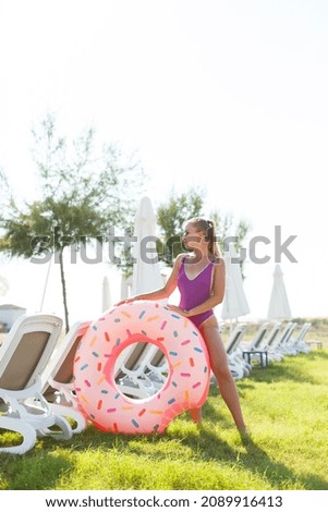A beautiful woman holds an inflatable circle in her hands, standing on the green grass. Attractive model with perfect body. Vacation concept, the girl goes to swim in the sea