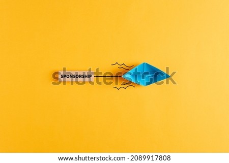 Paper boat pulls a wooden banner with the word sponsorship. Sponsoring, financial support or fundraising concept. Royalty-Free Stock Photo #2089917808