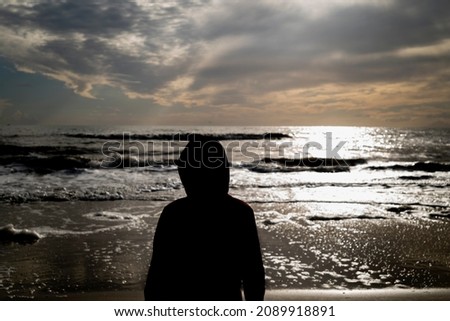 human silhouette picture looks at horizon on beach at sunset in sea water  