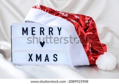 Lightbox with text MERRY XMAS with santa hat on silk fabric background. Winter holiday concept. Christmas and New Year