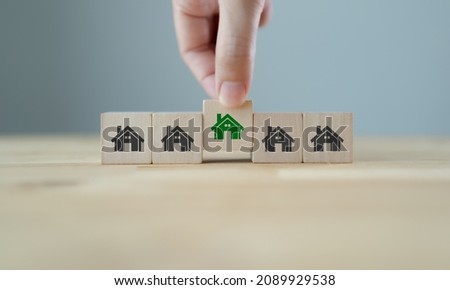 ECO house concept. Smart and sustainable design. Environmentally friendly house. Hand holds wooden cubes with green house symbols on grey background and copy space. Green and sustainable city banner.